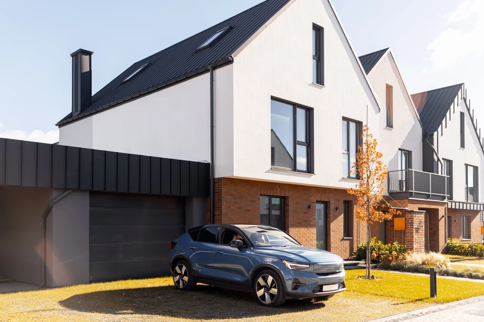 Scène extérieure résidentielle avec personne utilisant une télécommande pour ouvrir une porte de garage sectionnelle blanche en cours d'ouverture